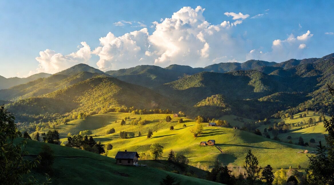 Extra Time on Wears Valley Cabin Moves | Mitchell Moving Serene panoramic view of Wears Valley in the Great Smoky Mountains, Tennessee, showing peaceful rustic log cabins nestled among lush green forests and rolling hills under warm golden hour sunlight.